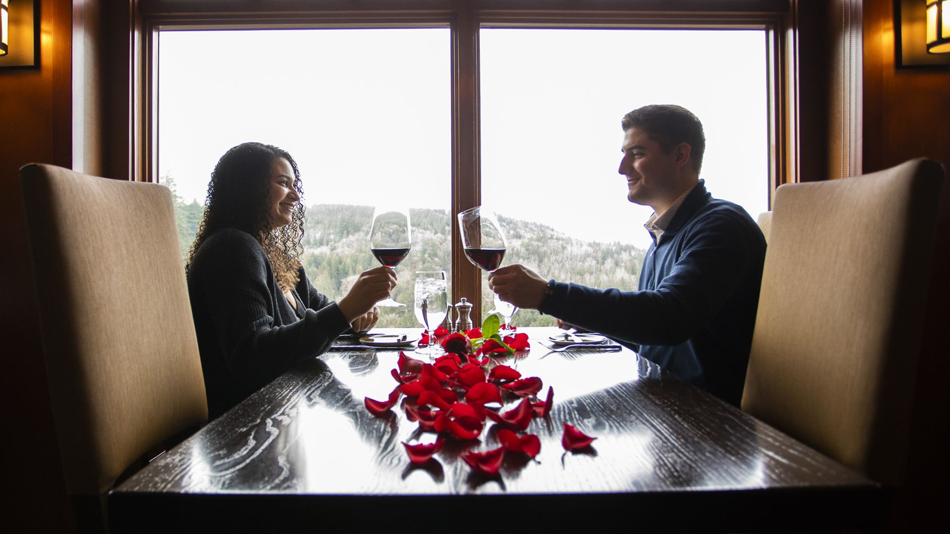A Man And Woman Sitting At A Table With Wine Glasses